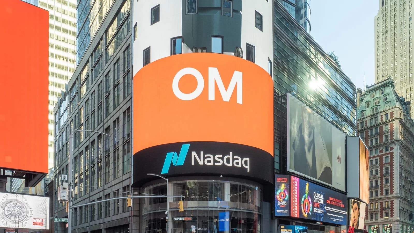 Die runde Eckfassade des Nasdaq MarketSite am Times Square in New York mit der großen LED-Wand und dem Nasdaq-Logo, davor Straßenverkehr, Polizeifahrzeuge und Passanten